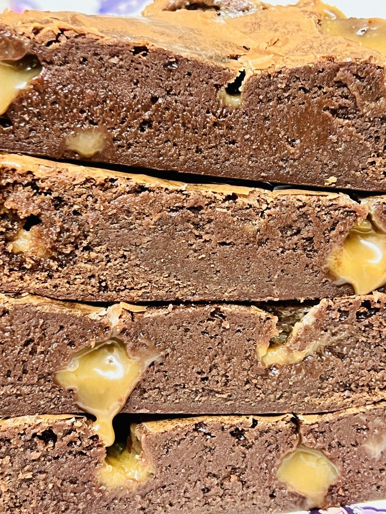 Four Salted Caramel brownies in a stack. The caramel is spilling out of the brownies enticingly.